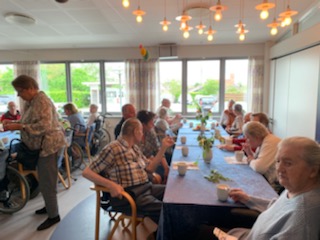 Beboere og pårørende sidder ved borde og drikker Irish coffee i cafeen på Solgården