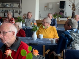Beboere og pårørende sidder ved borde og drikker Irish coffee i cafeen på Solgården